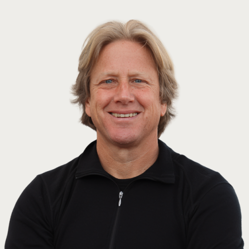 A middle-aged man with blonde hair wearing a black zip-up jacket, smiling at the camera against a plain white background.
