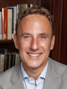 A man smiling in front of a bookcase.