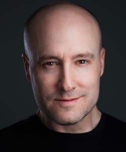 A bald man in a black shirt is posing for a photo.