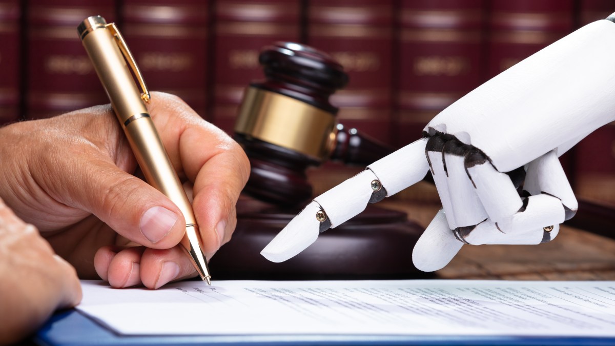 A robot hand helps a human hand sign a law document.