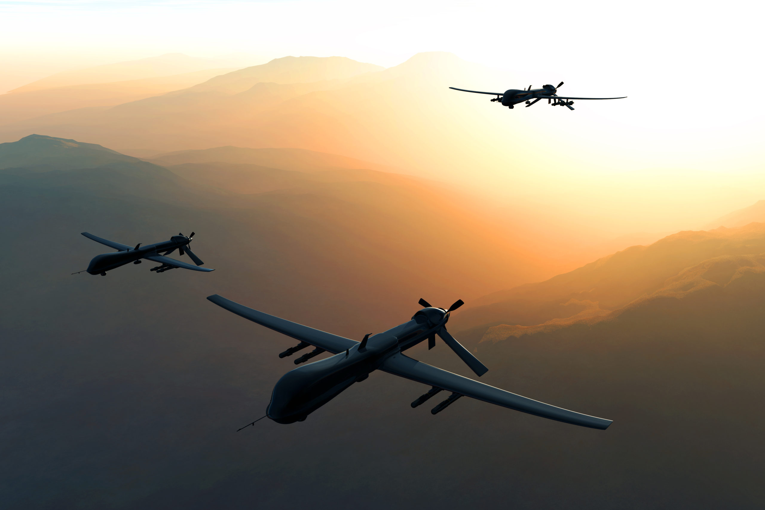 Three drones fly through sky with the sun behind them.