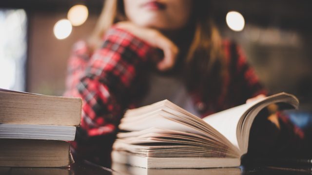 A woman stares pensively while reading a book.