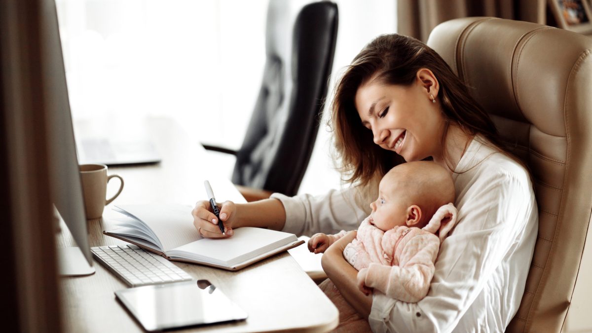 A working mom makes notes while holding her daughter.