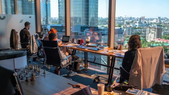 The future of work illustrated by four colleagues sitting at a long table by a window.
