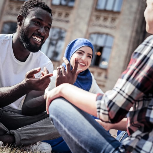 A man has a conversation with two women on a college green.