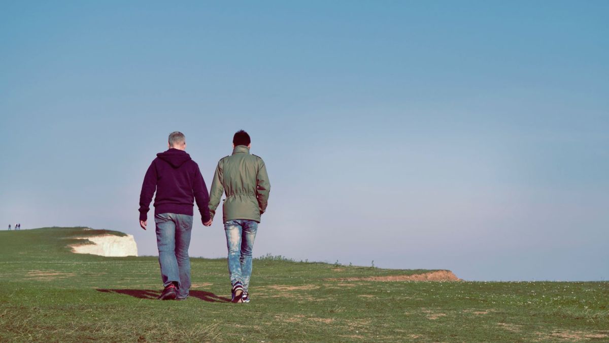 Two men holding hands on a grassy cliff.