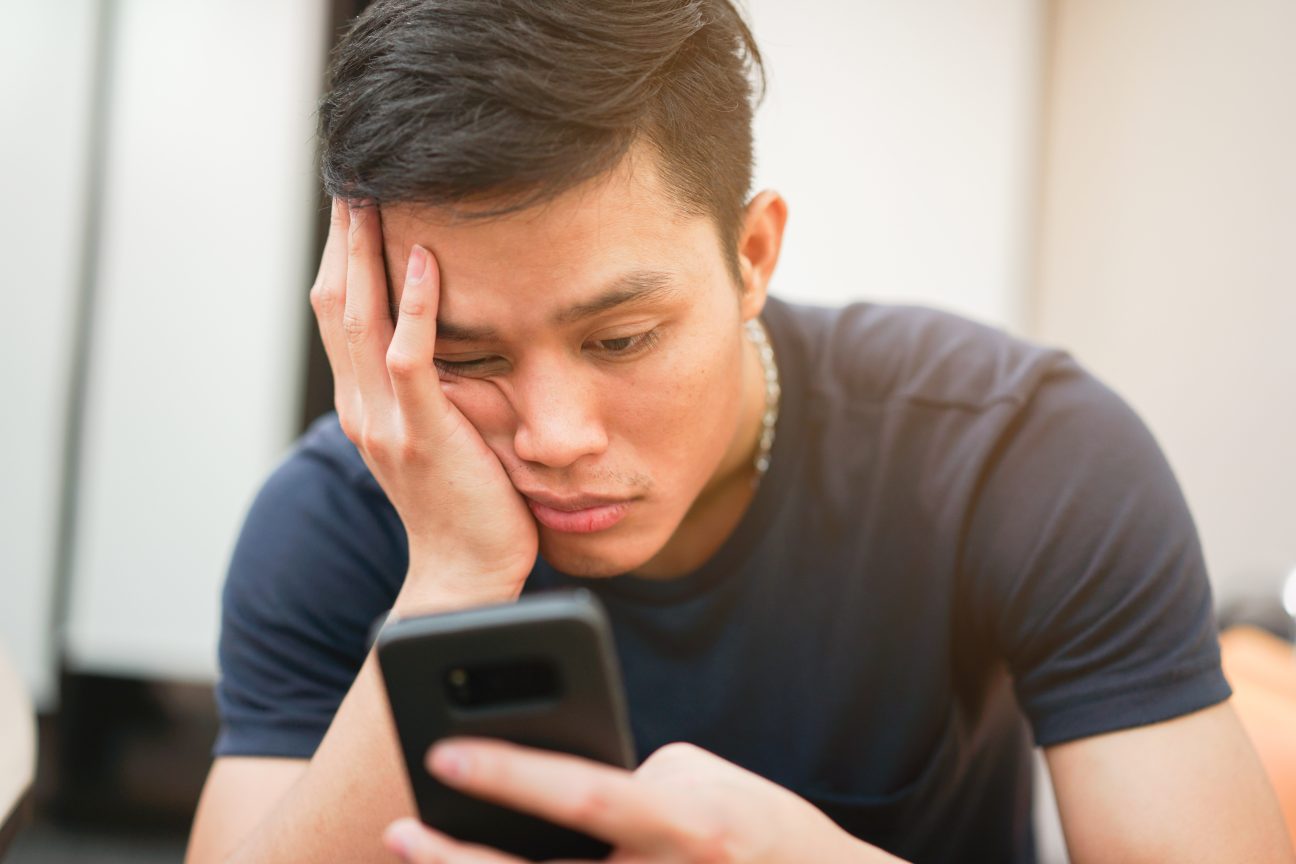 A man looks at his phone, seeking a digital distraction because he's bored.