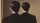 A man in a suit stands facing a mirror, but the reflection shows the back of his head instead of his face.