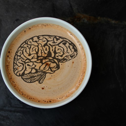 A cup of coffee with a brain silhouette drawn on the foam.