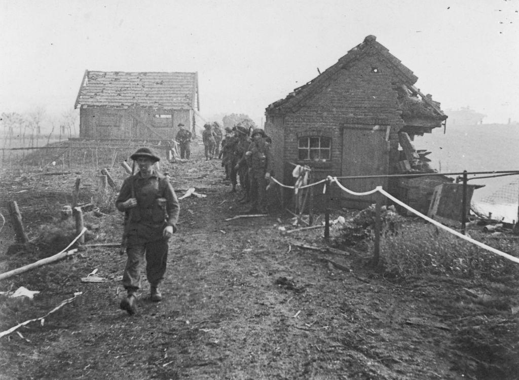 An old, black-and-white photograph depicting a British soldier walking in front of a dilapidated building.
