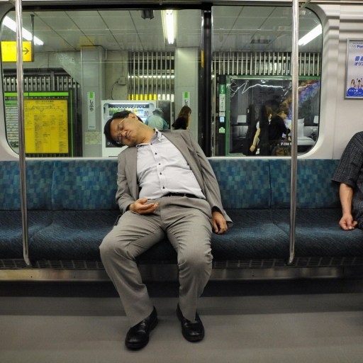 Two Japanese men sleep on a train car.