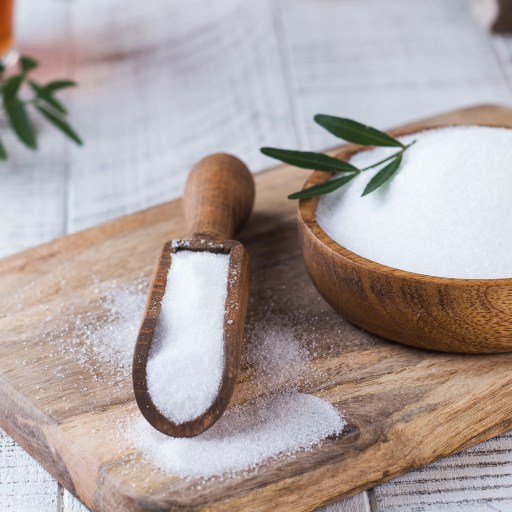 a wooden bowl filled with erythritol next to a wooden spoon.