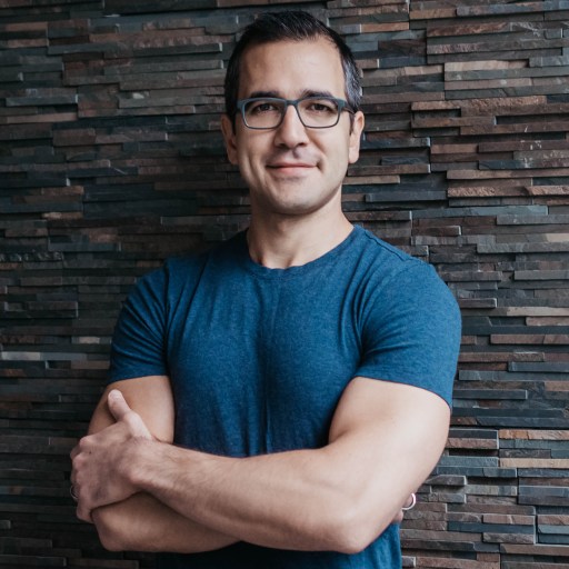 a man wearing glasses standing in front of a brick wall.
