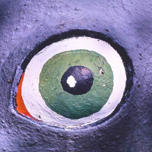 Close-up of a painted eye on a textured surface, featuring green, white, black, and a small area of orange.