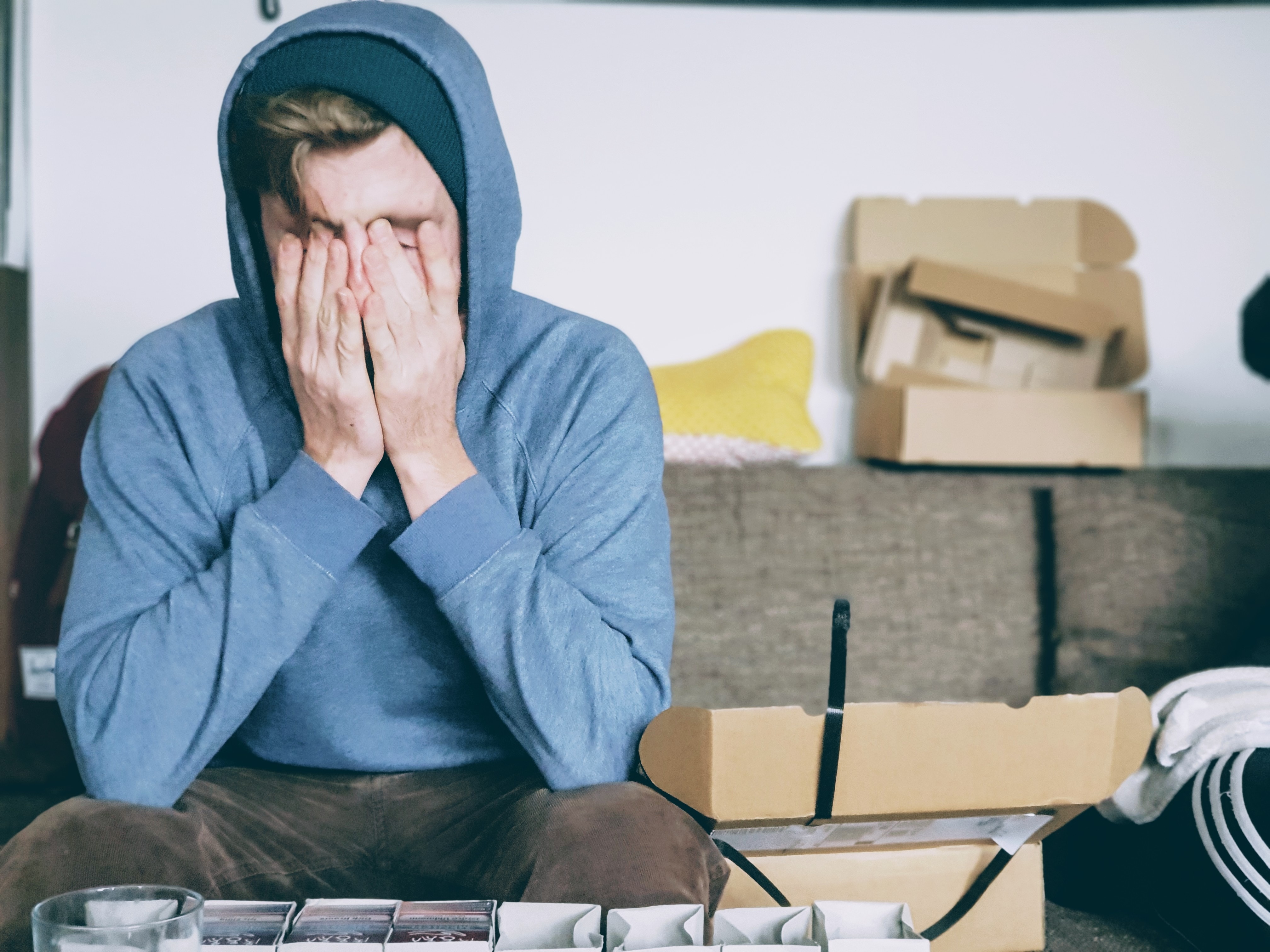 A man sitting on a couch covering his face with his hands.