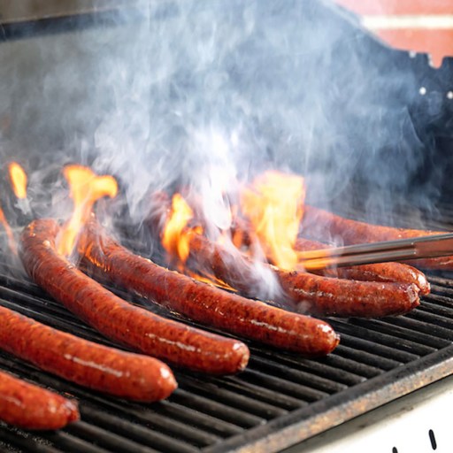 a person cooking hot dogs on a grill.