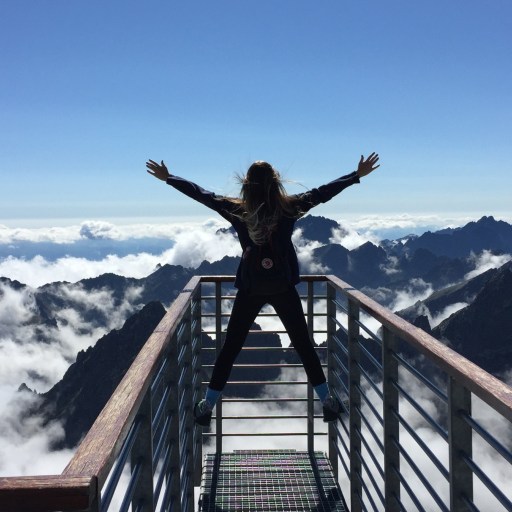 A woman standing on top of a metal railing above a mountain range.