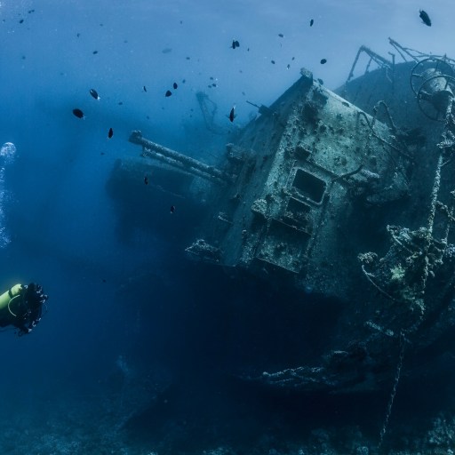 a man scubas near a ship in the ocean.