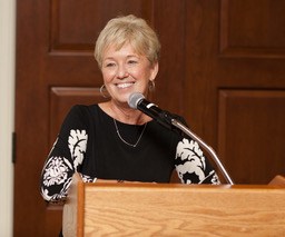 A woman smiles at a podium while giving a speech.