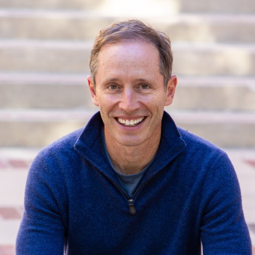 a smiling man sitting in front of some steps.