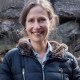 a woman in a black jacket standing in front of a rock.