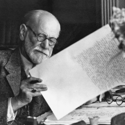 an old man sitting at a desk reading a book.