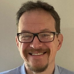 a smiling man wearing glasses and a blue shirt.