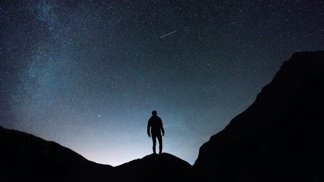 a person standing on top of a mountain under a starry sky.