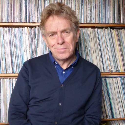a man sitting in front of a shelf full of records.
