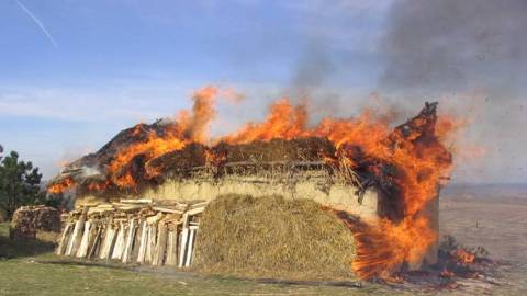 A burning house in a field.