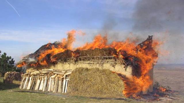 A burning house in a field.