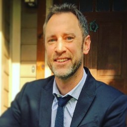 A man in a suit and tie smiling in front of a door.