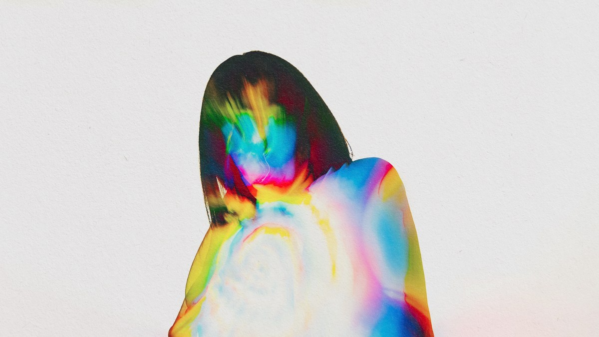 A woman in a vibrant dress is standing against a minimalist backdrop.