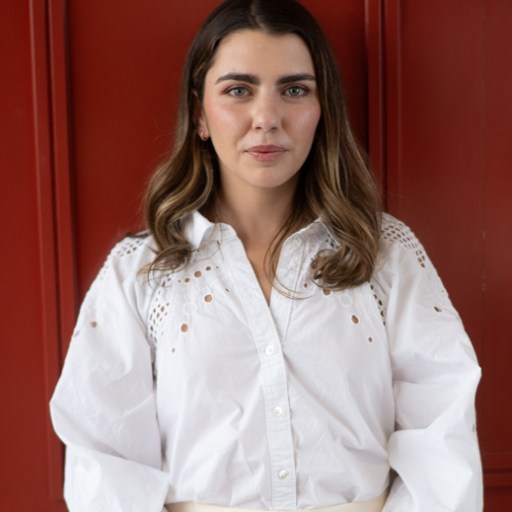A woman in a white shirt and white pants standing in front of a red door.