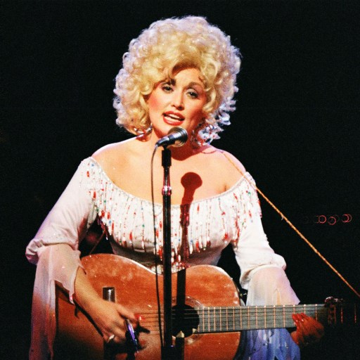 Dolly Parton on stage with an acoustic guitar showcases her musical talent.
