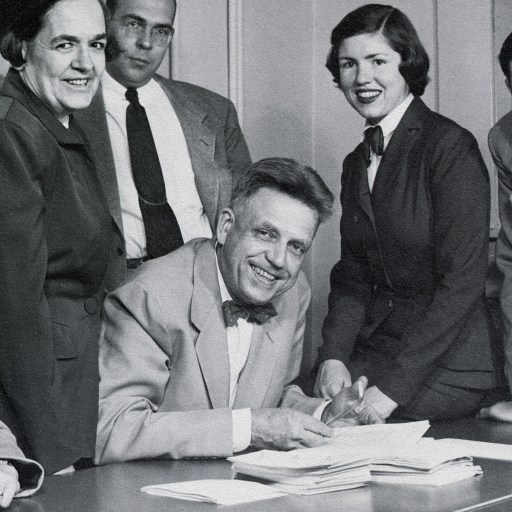 A group of people sitting around a desk signing papers during a Kinsey study.