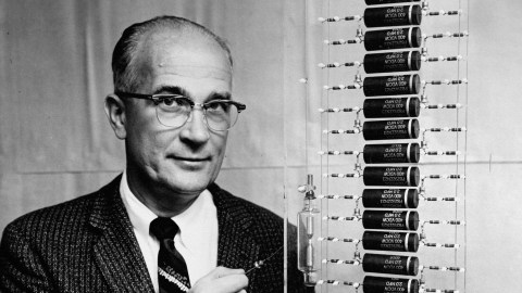 A man in a suit standing next to a display of batteries showing signs of "nobel disease.
