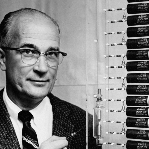 A man in a suit standing next to a display of batteries showing signs of "nobel disease.