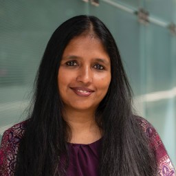 A woman with long black hair standing in front of a glass wall.
