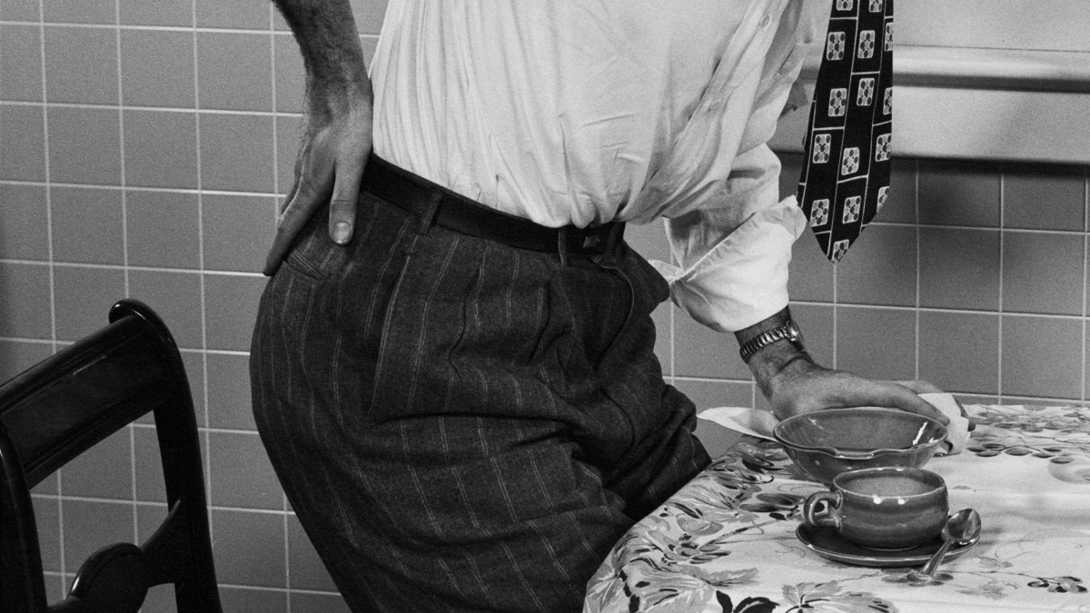 A man sitting at a table with a cup of tea, experiencing chronic pain.