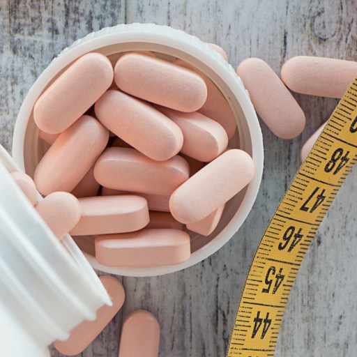 A measuring tape alongside a bottle of exercise pills on a wooden table.