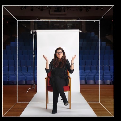 An image of a woman sitting in a chair in front of an auditorium.