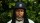 A man with dreadlocks standing in front of a bush.