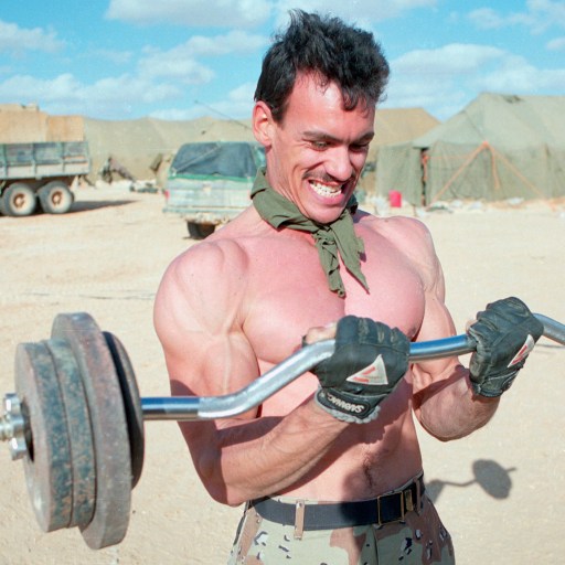 A man showcasing his strength by lifting a barbell in the barren desert.