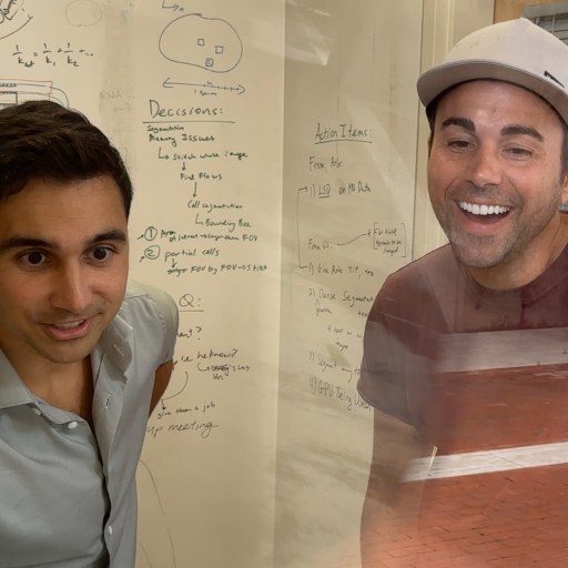 Two men smiling in front of a white board.