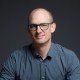 A bald man wearing glasses and a blue shirt.