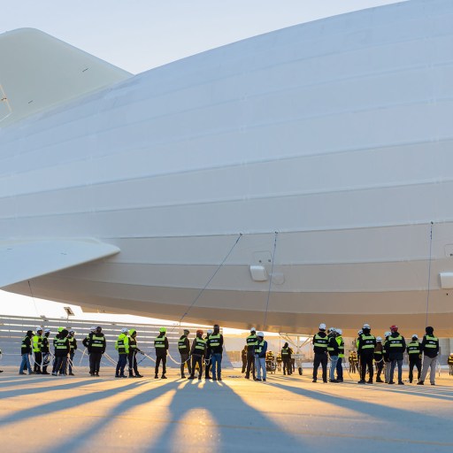 A group of people standing in front of a large white blimp.
