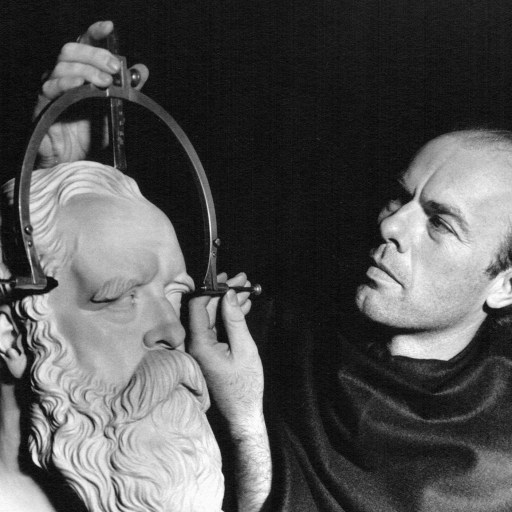 An old black and white photo of a man practicing phrenology on a bust.