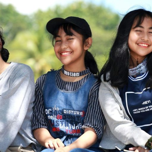 Three young girls sitting on a bench and smiling.