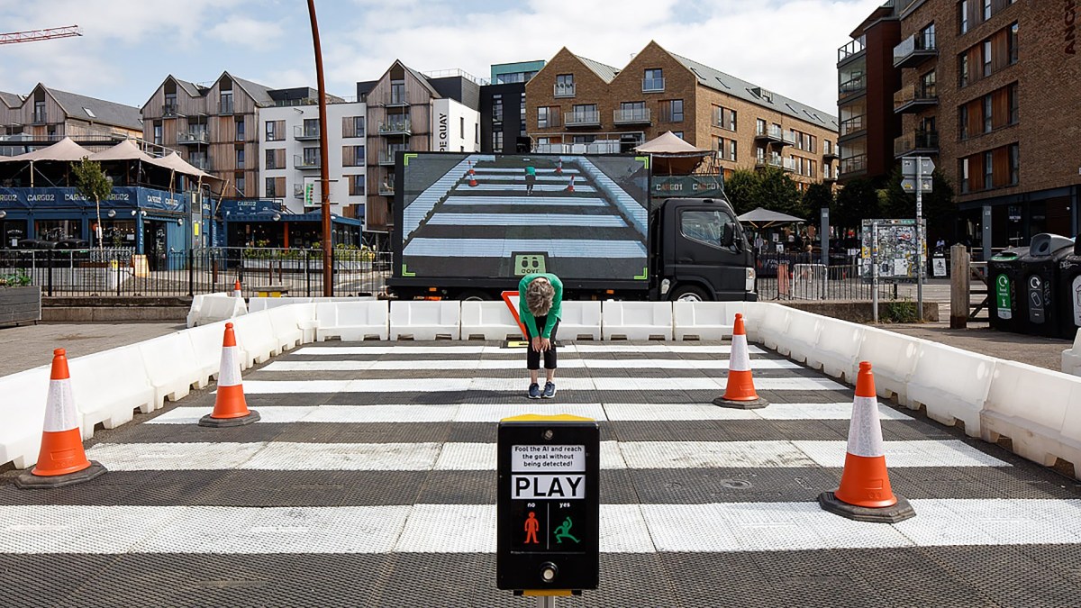 A man is crossing a street with cones in front of him.